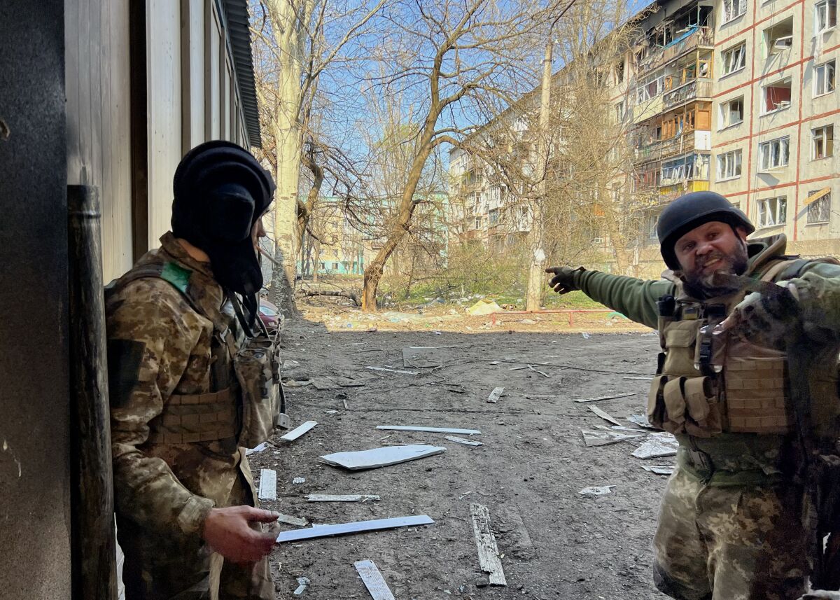 Bir binanın gölgesinde duran iki asker, biri işaret ediyor  