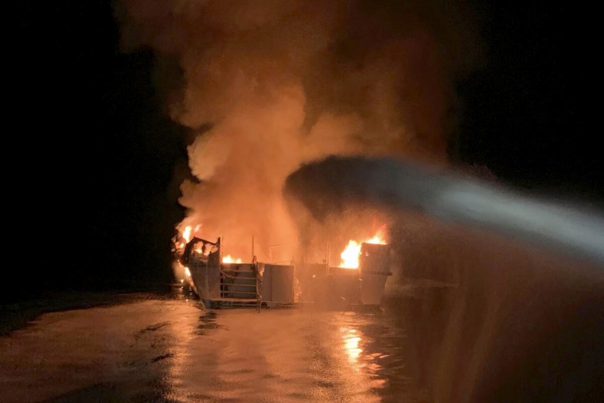 Water is sprayed on a burning boat at night