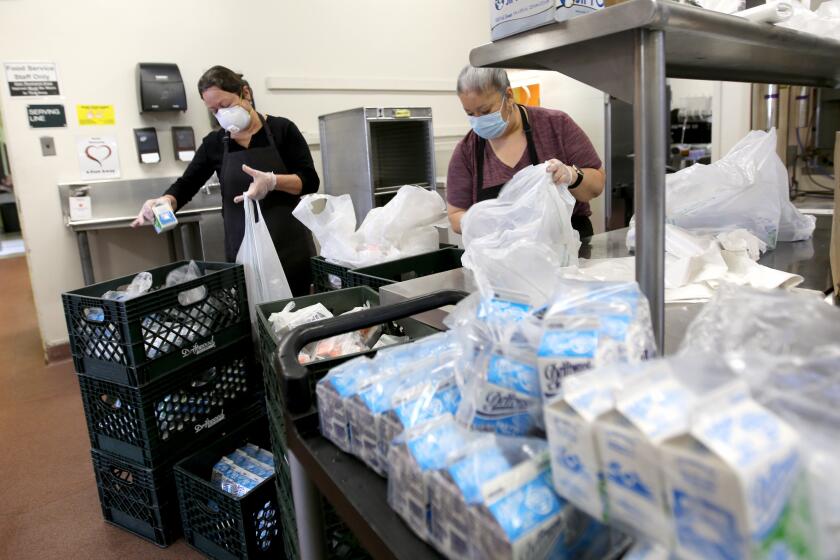 Burbank Unified cafeteria workers Carmen Cezena, left, and Norma de la Torre, right, prepare milk and juice bags for the five-day meal packages for students across the district, at Burbank Middle School on Tuesday. March 24, 2020.
