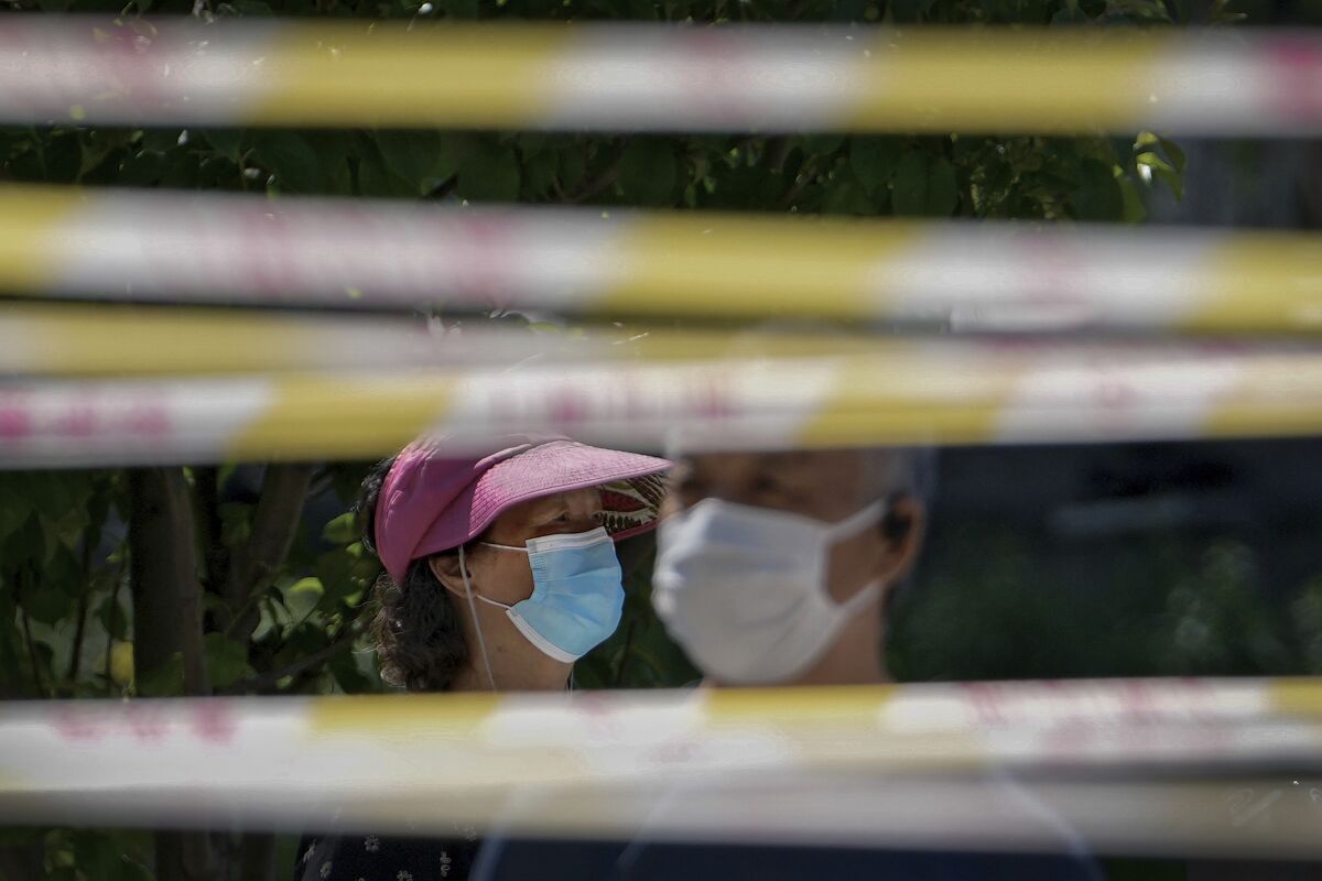 Residents wearing face masks line up behind barricaded tapes for COVID mass testing near a residential area on Sunday, May 15, 2022, in Beijing. (AP Photo/Andy Wong)