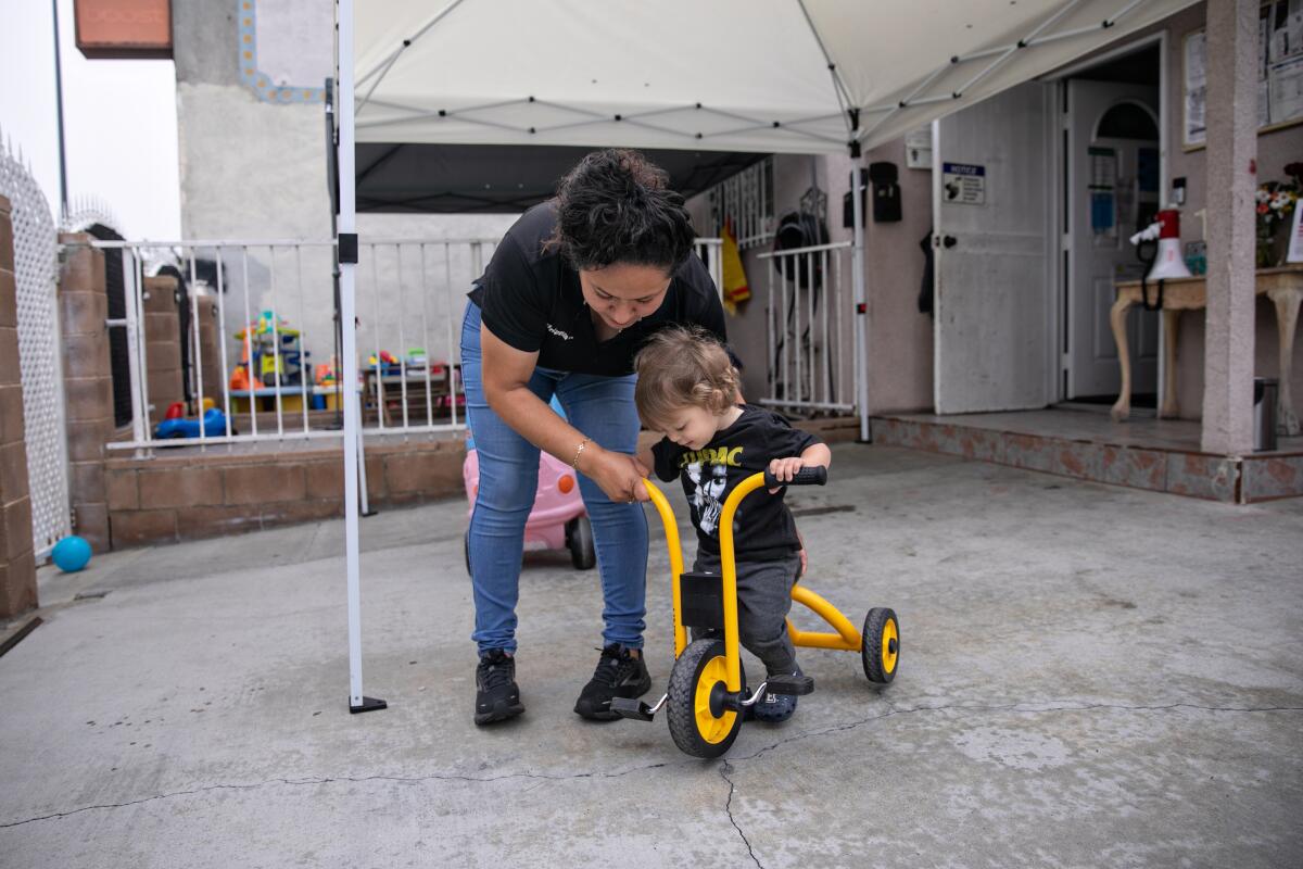Adriana Lorenzo helps a toddler ride a tricycle.