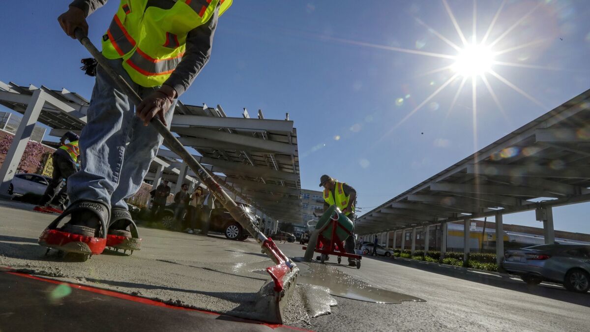 Juan Reyes, left, and Devin Vestal apply a cool pavement material to a parking lot in downtown Los Angeles. City officials hope the pavement will help cool the city and mitigate the effects of climate change.
