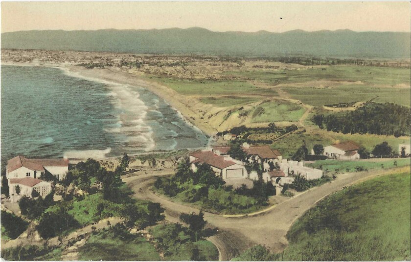 Houses on a bluff above the ocean, with sand and surf stretching into the distance