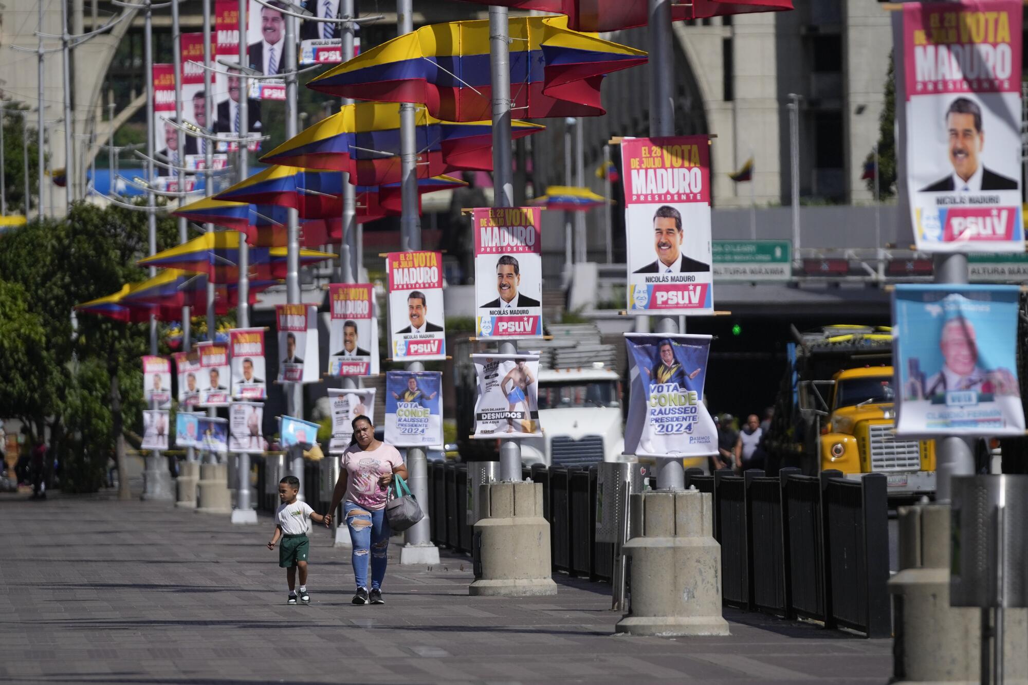 Una mujer y su hijo caminan por una calle llena de carteles de campaña que promocionan 
