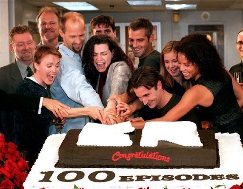 In this Oct. 20, 1998 file photo, cast members, front row from left, Laura Innes, Anthony Edwards, Julianna Margulies, George Clooney, Noah Wyle, Kellie Martin, and Gloria Reuben, cut a cake celebrating the 100th episode of the NBC series, "ER," as NBC President Warren Littlefield, second row left, and series creator John Wells, look on. (AP Photo/Rene Macura, file)