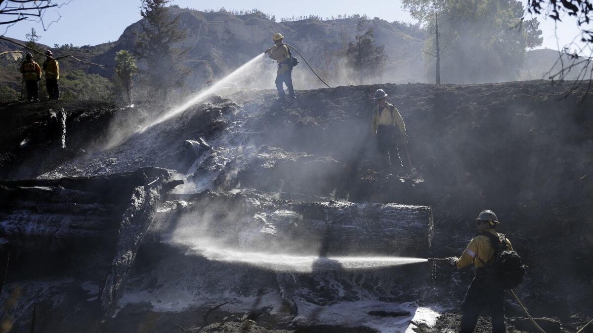 Firefighters hose down hot spots created by a brush fire Oct. 19 in Santa Paula, Calif.