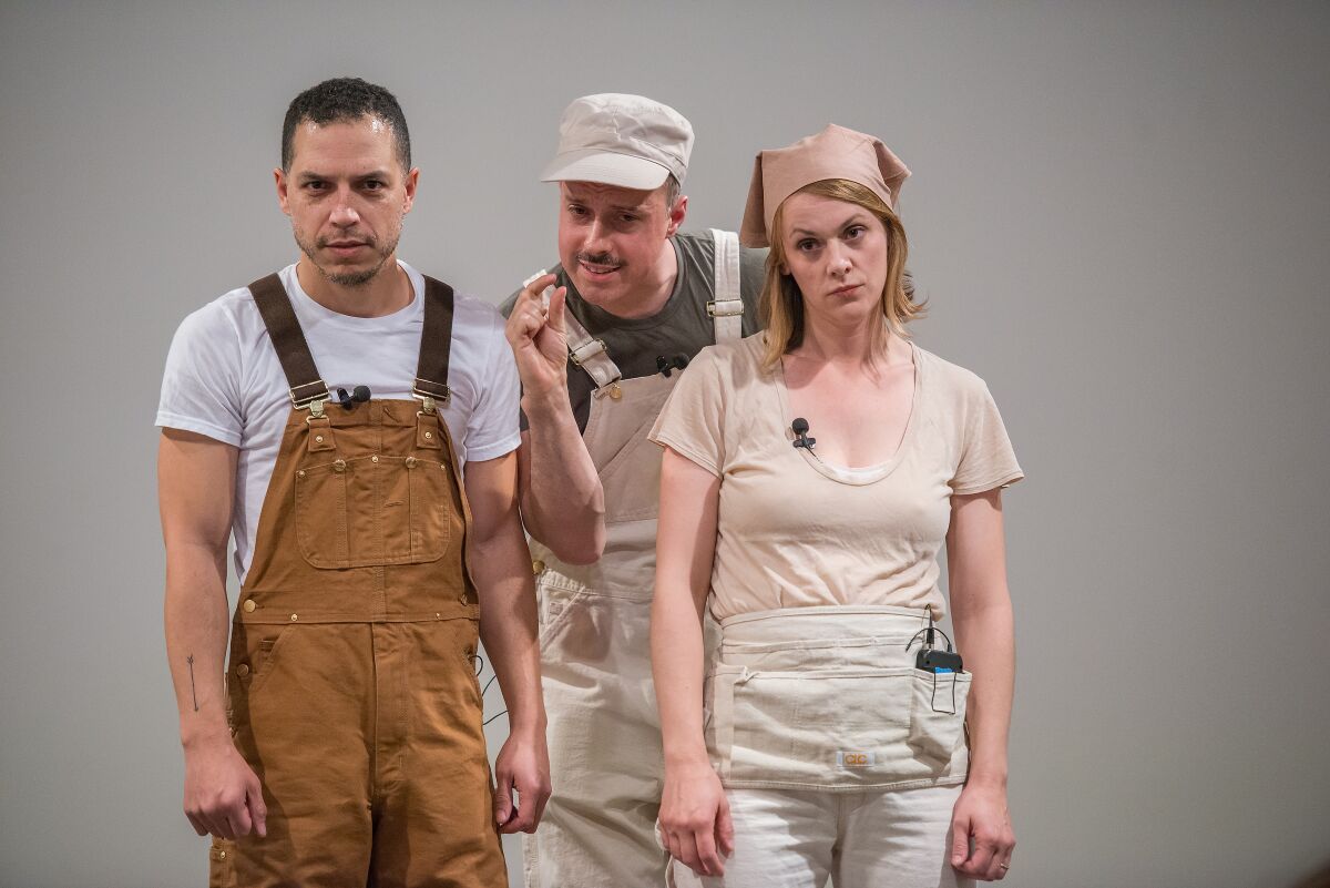 Two men in overalls and a woman in kerchief and painter's apron stand on a stage.