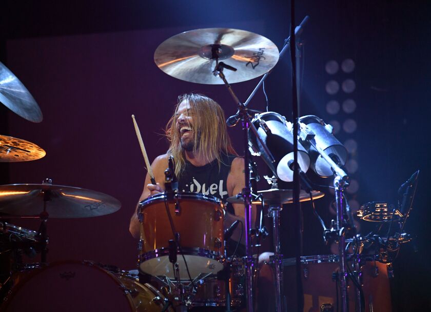 A man with long blond hair plays the drums