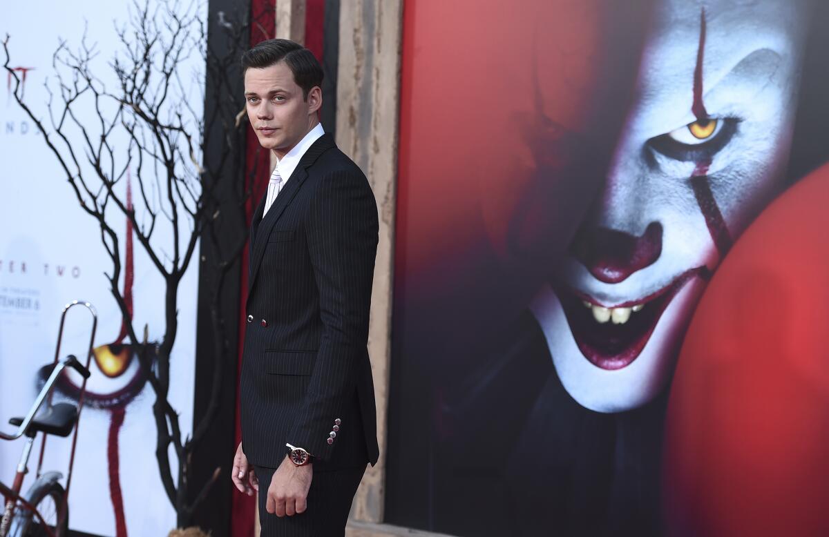 A man in a suit standing in front of a giant poster with a scary clown face on it
