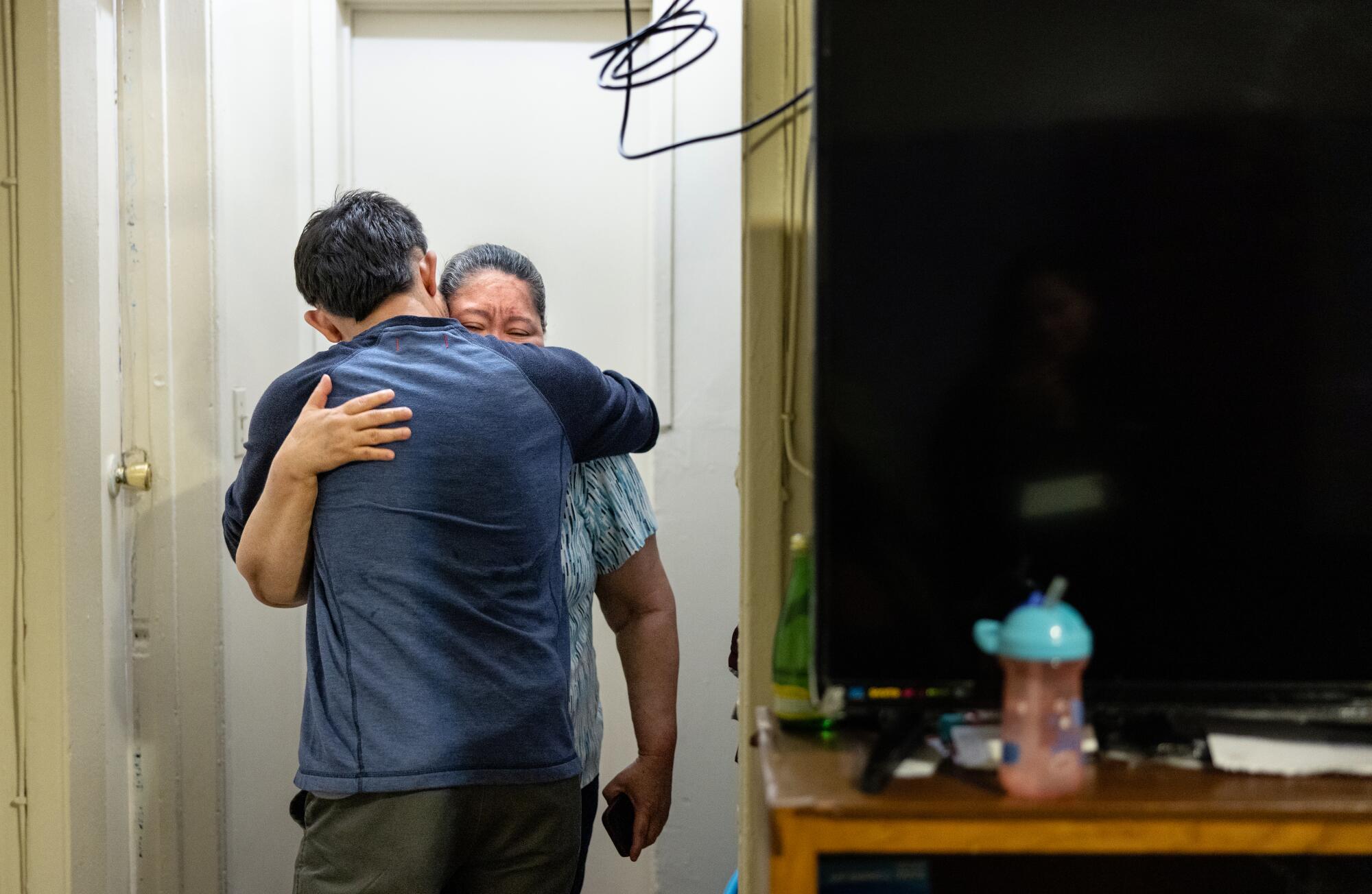 A woman hugs a man while crying and holding her cellphone