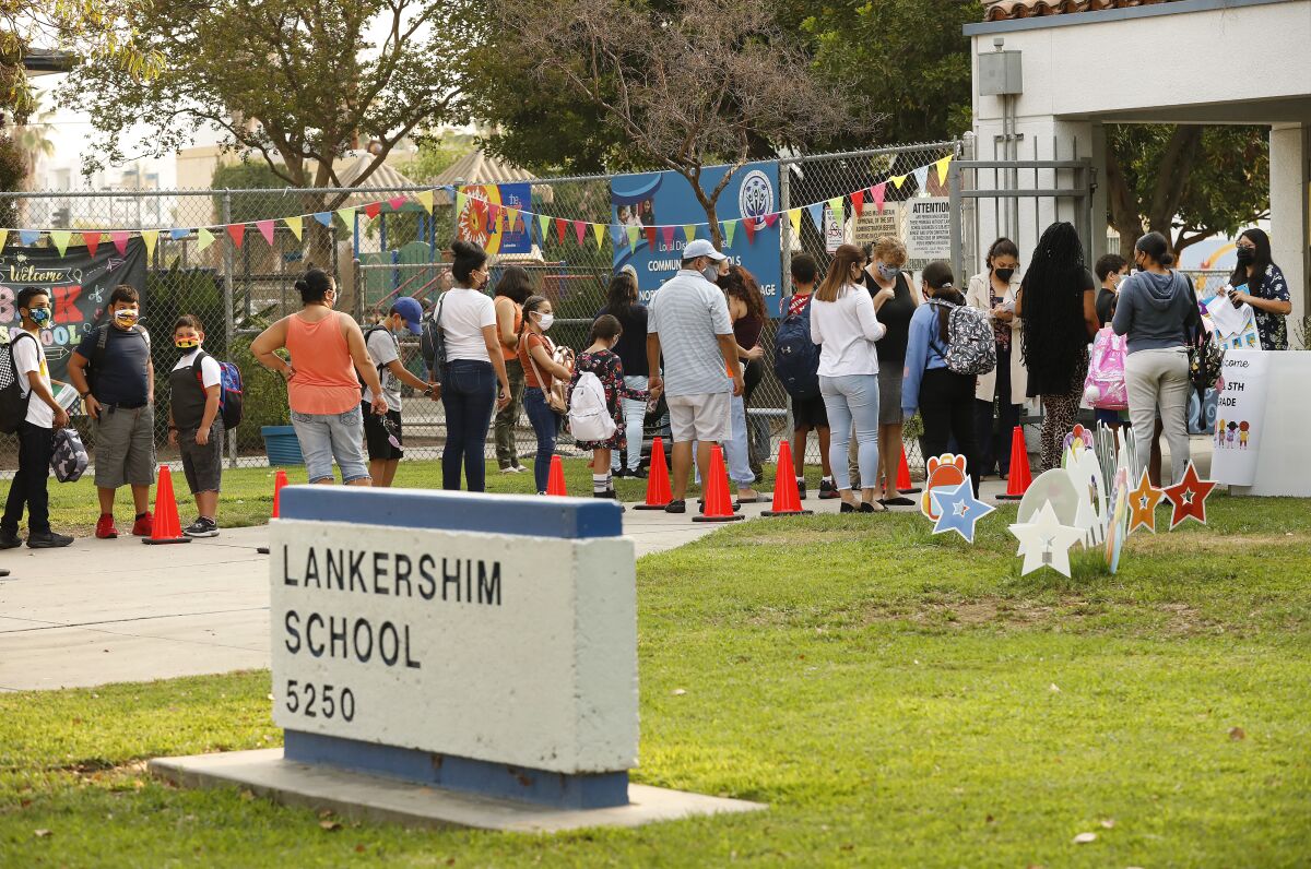 Parents and students stand in line outside a school. 
