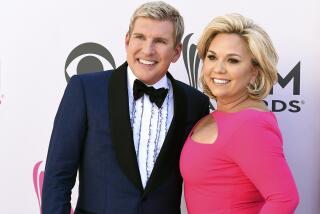 Todd Chrisley in a tuxedo smiling and posing next to Julie Chrisley in a hot pink gown