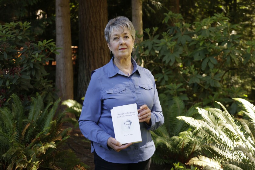 A woman standing among ferns and shrubs holds a pair of books.