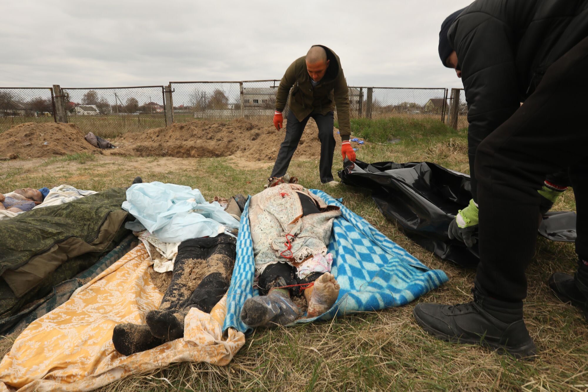 Two men lean over bodies wrapped in blankets  