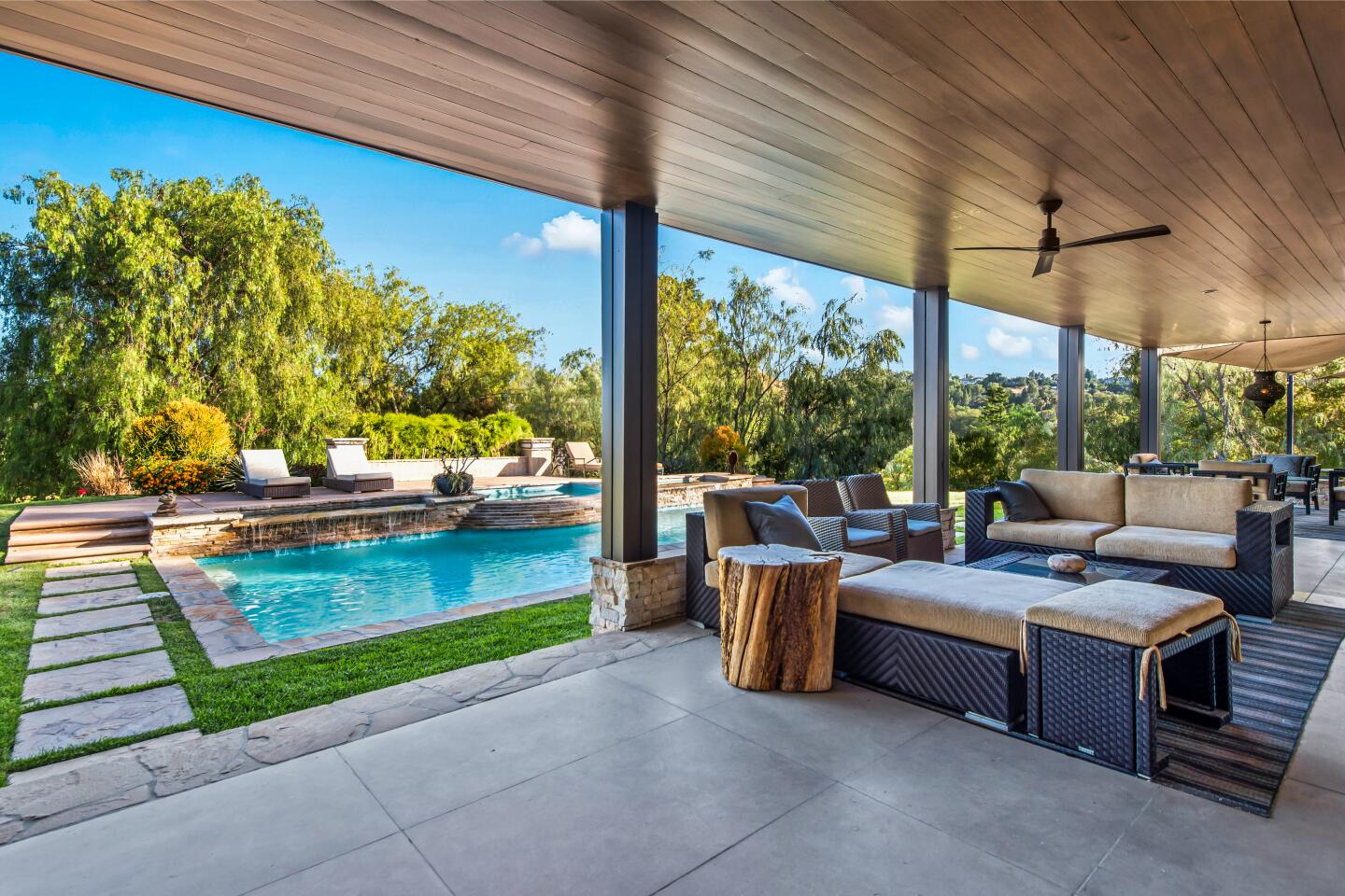 The patio has furniture, a pool nearby and trees in the background.