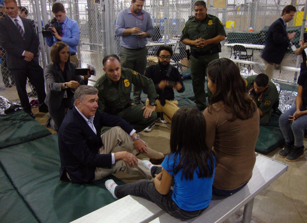 Border Patrol Commissioner R. Gil Kerlikowske, left, talks with a Salvadoran mother and her 6-year-old twins with the help of a Border Patrol agent's translation. Kerlikowske visited the processing center in McAllen, Texas, on Wednesday in an attempt to deter people from crossing the border.