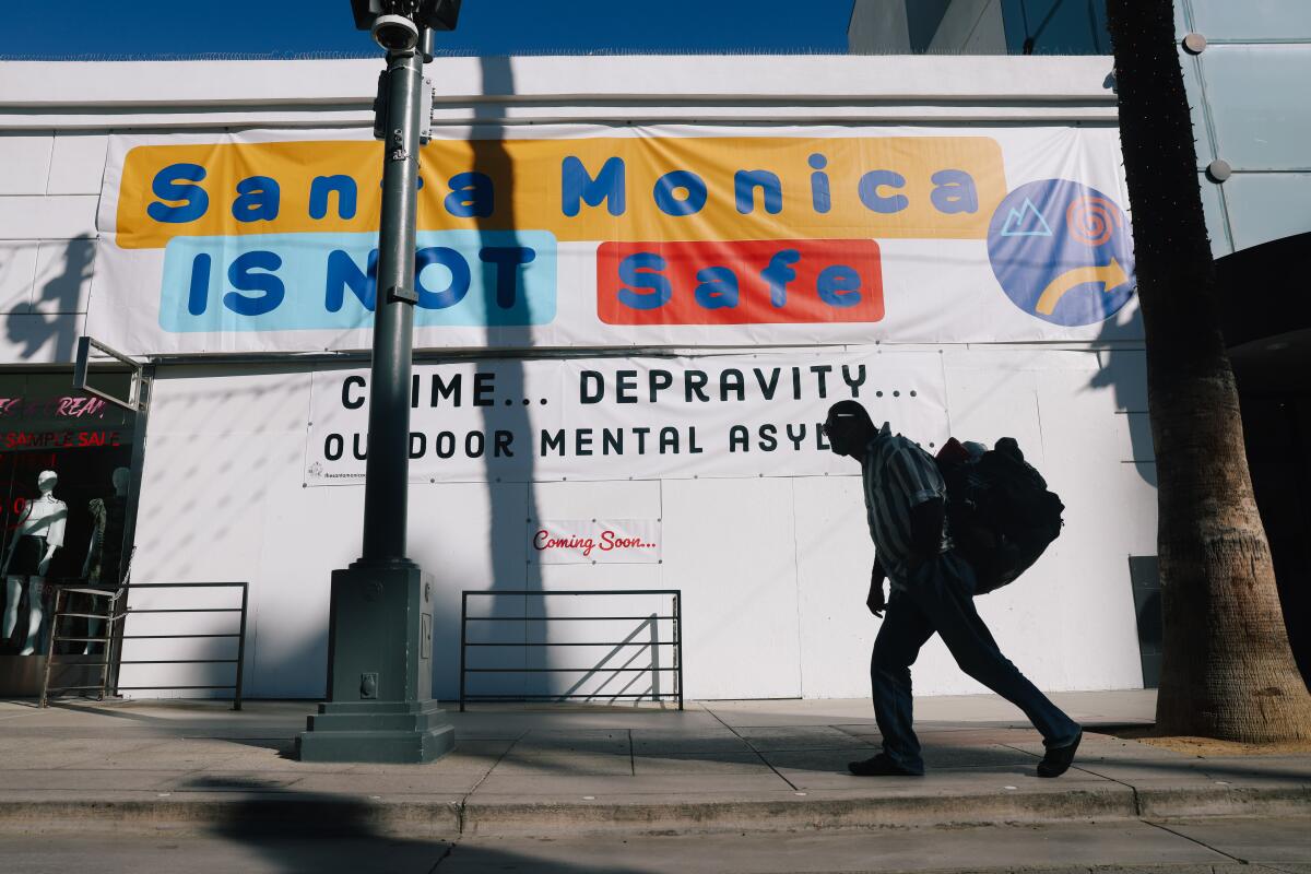 A yellow, blue and red sign reads "Santa Monica is Not Safe" on a building