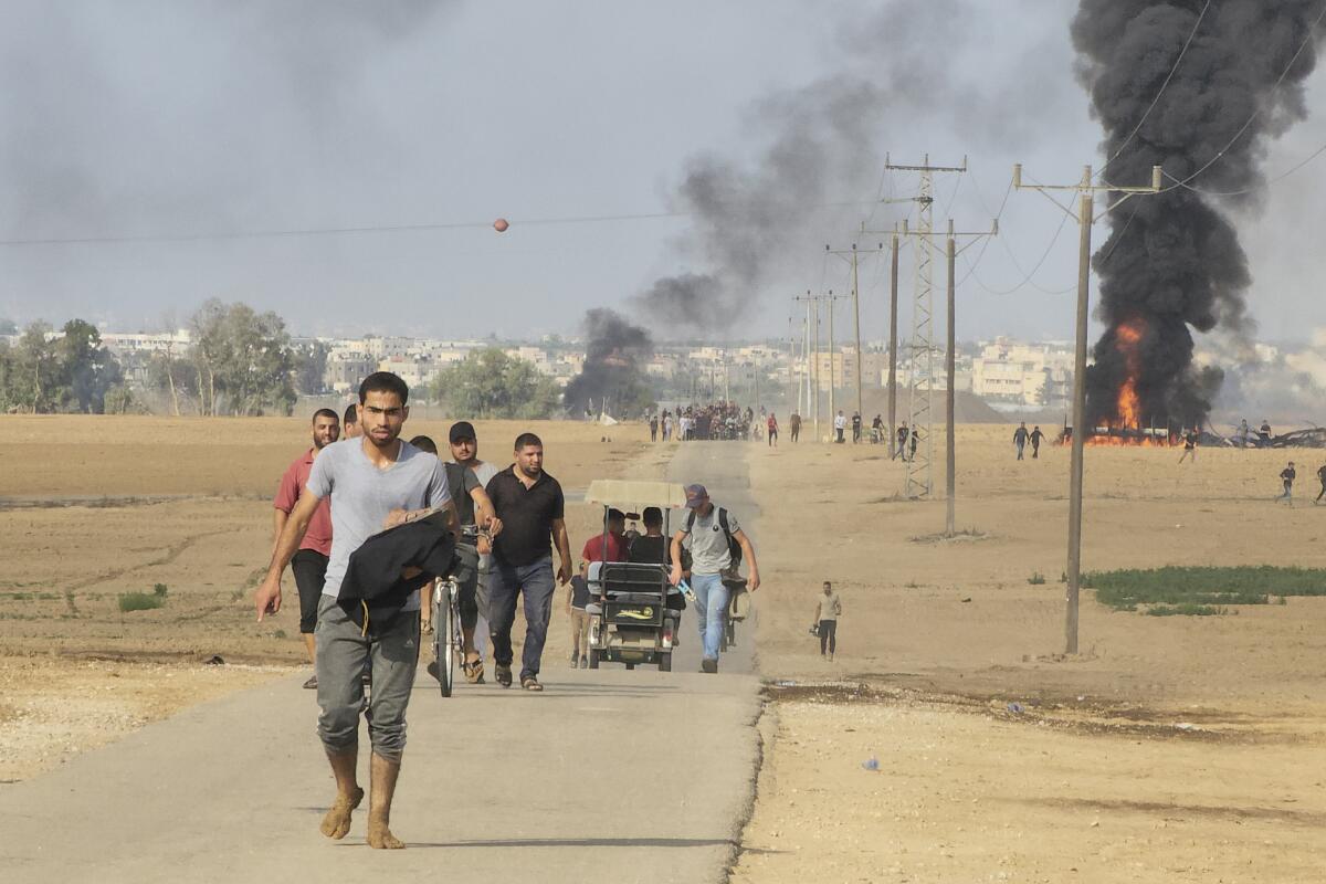 Palestinos se alejan del kibbutz de Kfar Azza, Israel, cerca de la cerca fronteriza de la Franja de Gaza.