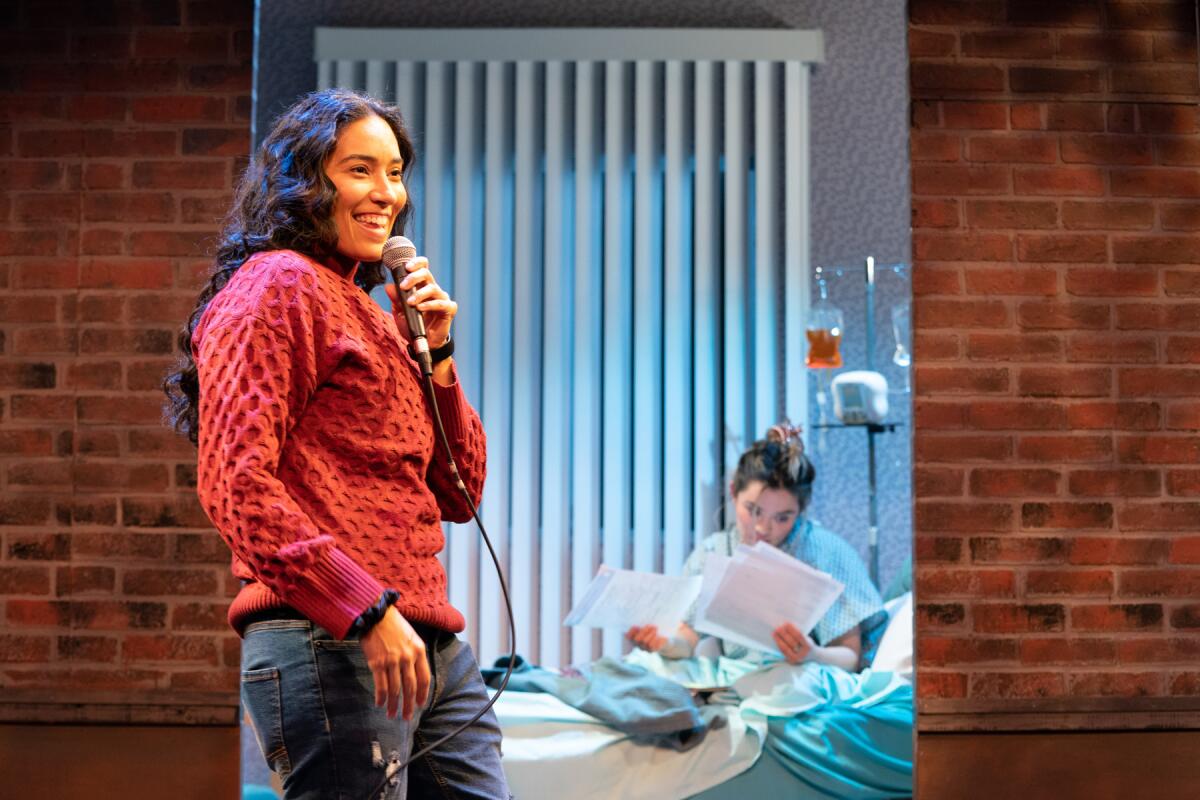 woman onstage with a mic and a picture of a woman in a hospital bed behind her