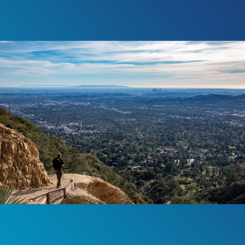 A hiker descends the Sam Merrill Trail with views of downtown Los Angeles.