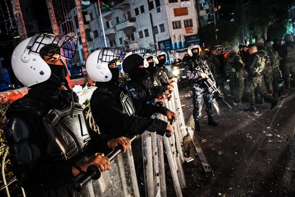 Riot police stand in a line holding shields.