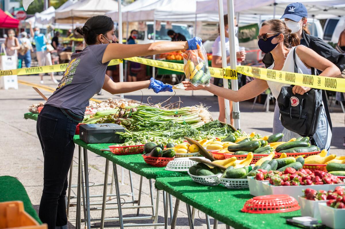 A woman hands a shopper a bag of vegetables at a Pacific Beach farmers market. 