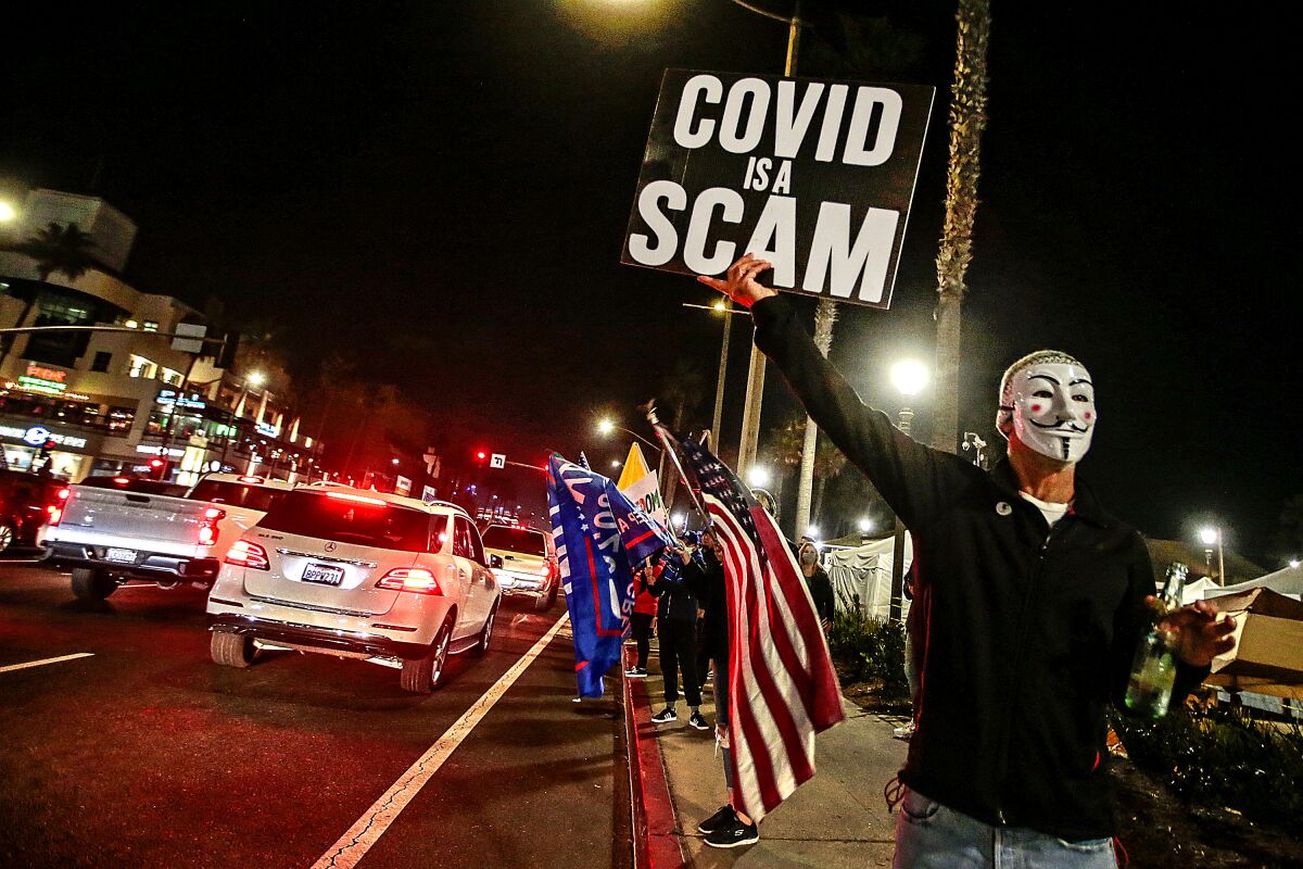A person holds a sign that says "COVID is a scam."