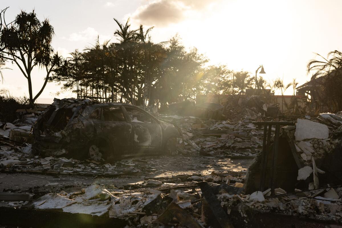 A burned-out car lies in the driveway of charred apartment complex in the aftermath of a wildfire in Lahaina