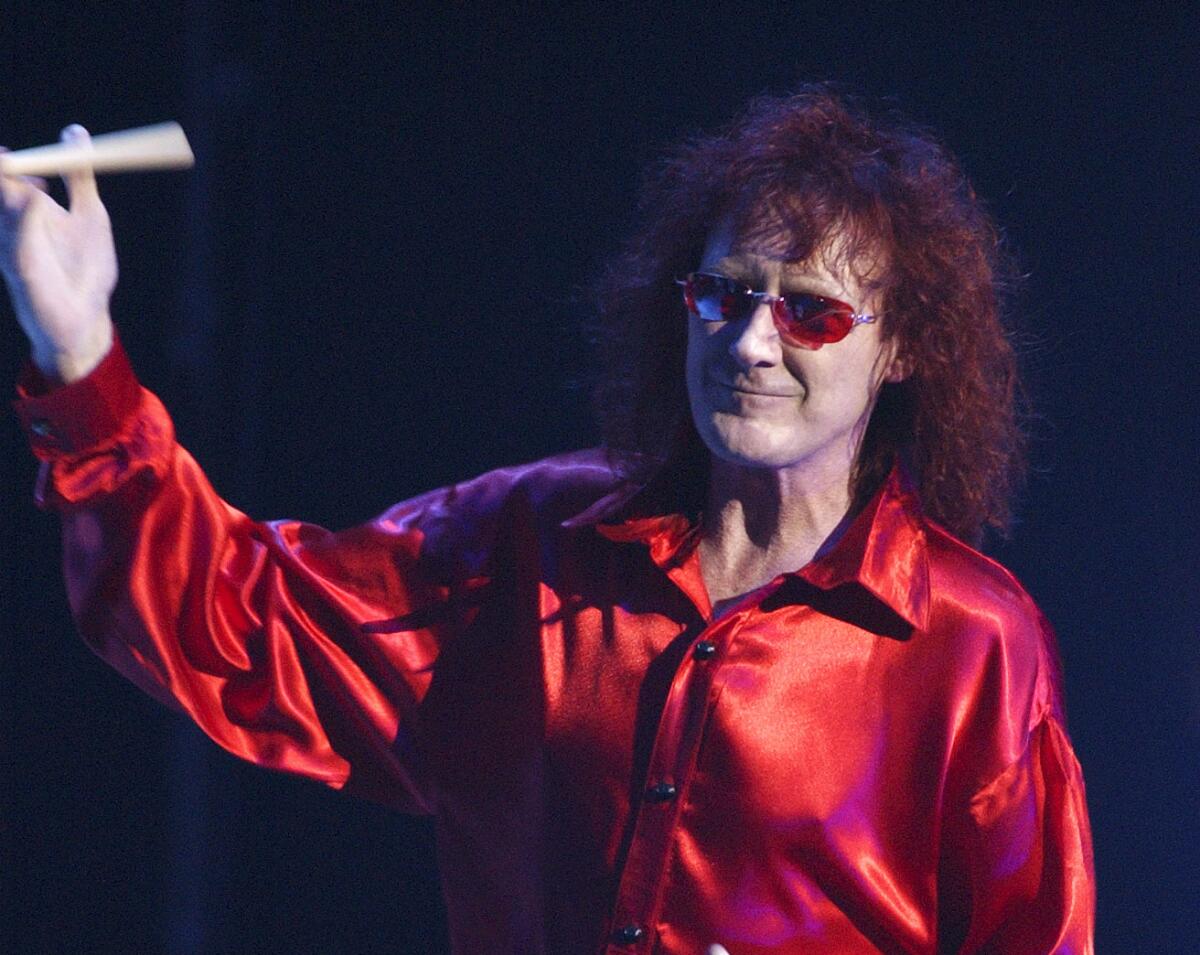  Colin Burgess in a red silk shirt and red glasses performs on stage.