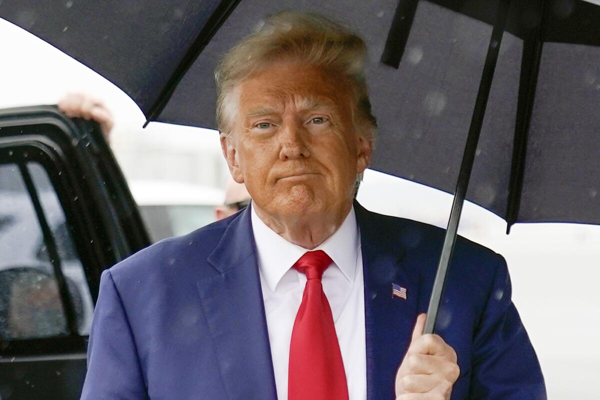 Former President Trump pictured from the shoulders up, holding an umbrella and standing near a black car