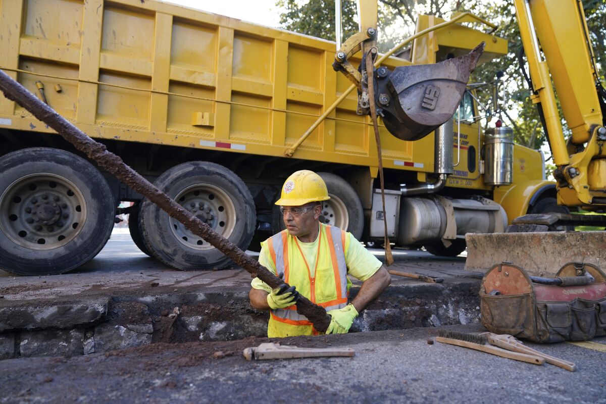 A worker removes an old water pipe from underneath the street
