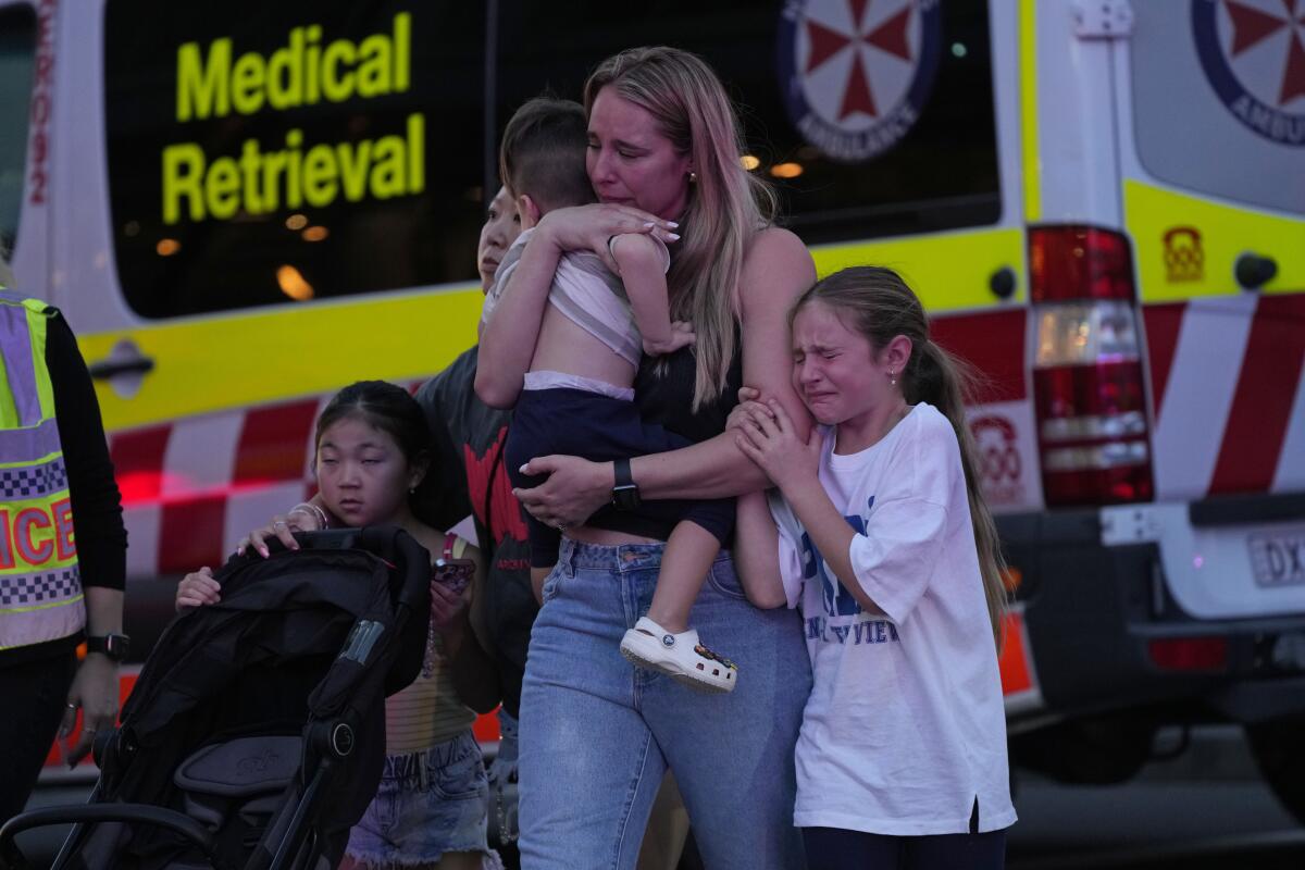 Two women hold or guide their children as they walk behind an ambulance. 