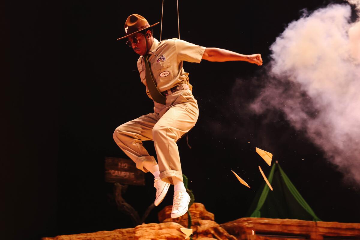 Tyler, the Creator at Coachella jumps in the air while wearing a khaki outfit and ranger hat.