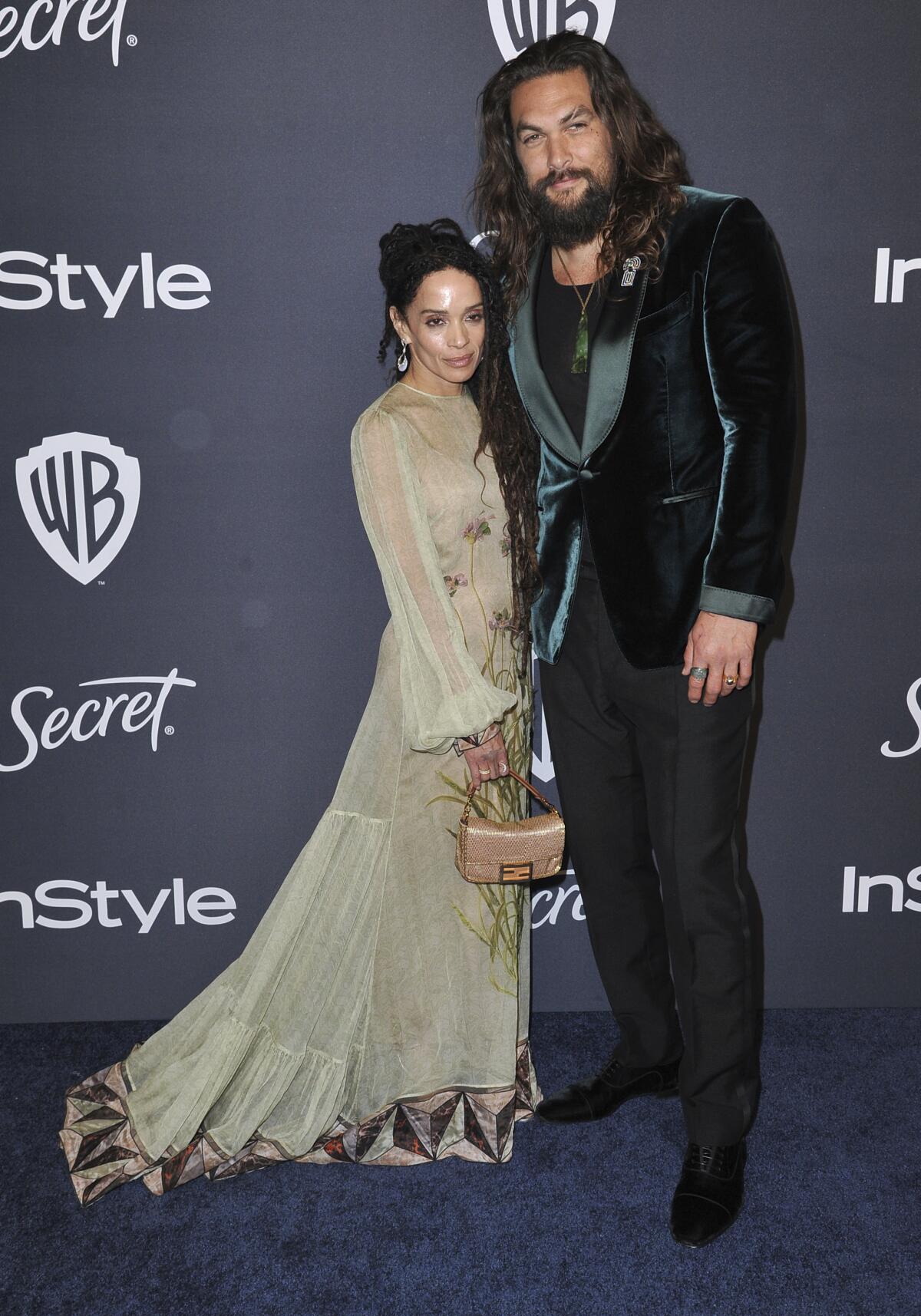 Lisa Bonet in a light green dress poses next to Jason Momoa in a green suede jacket, black pants and green shirt 