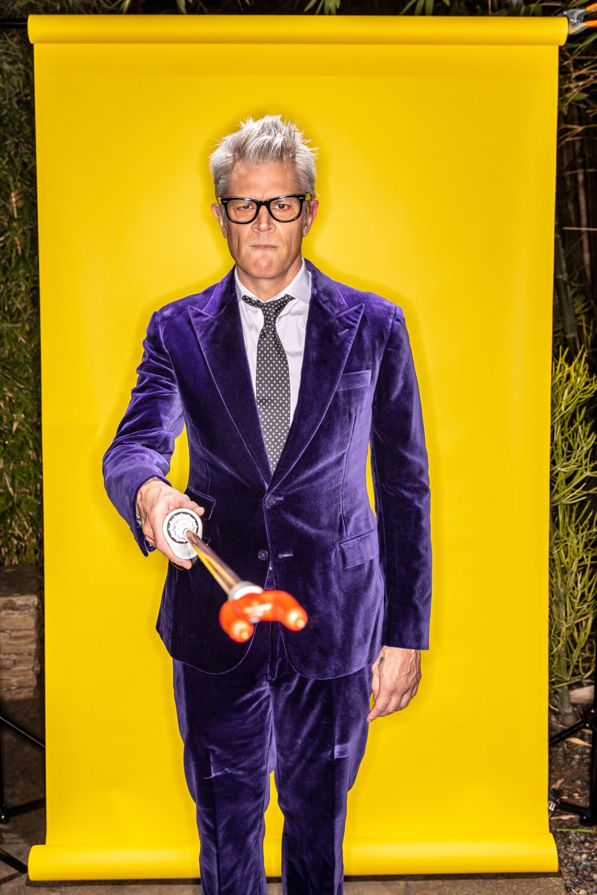 A man in a purple velvet suit holds out a shocker 