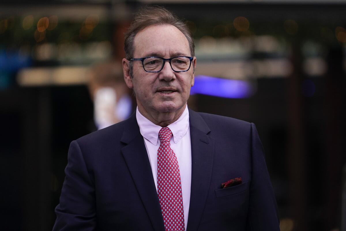 Kevin Spacey in glasses, a dark blue suit, red tie and a white shirt