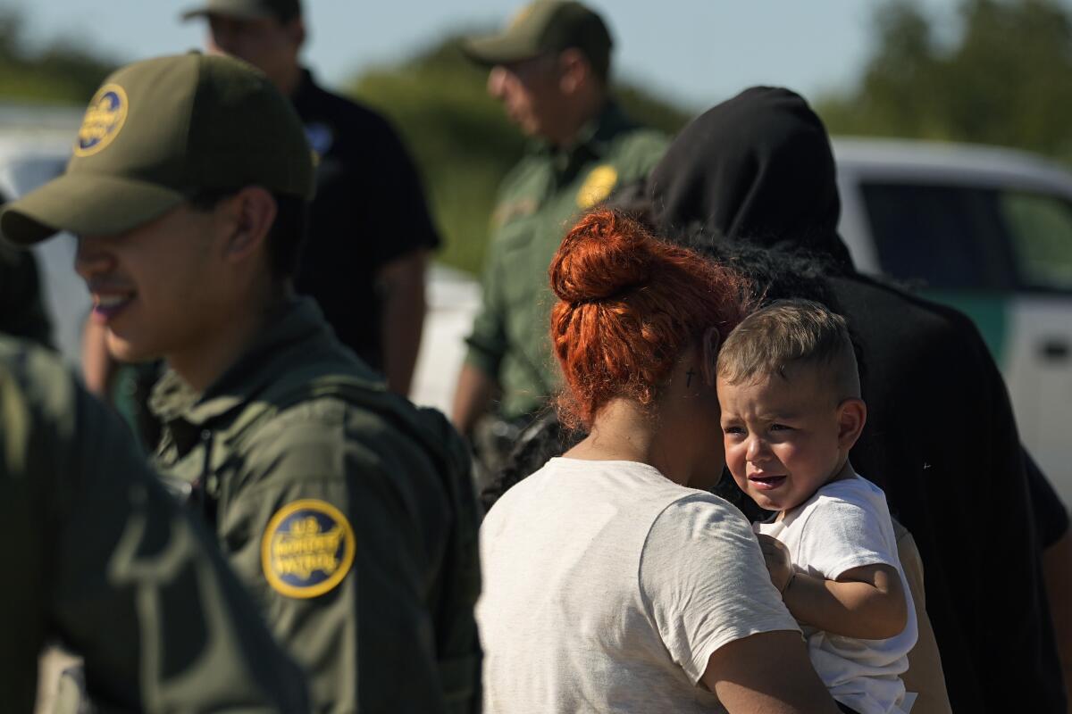 A woman holds a young child as men in Border Patrol uniforms surround them.
