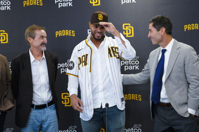 San Diego, CA - December 09: At press conference held at Petco Park on Friday, Dec. 9, 2022 in San Diego, CA., Xander Bogaerts tries on his Padres jersey and cap with Peter Seidler (l) and A. J. Preller (r) looking on. (Nelvin C. Cepeda / The San Diego Union-Tribune)