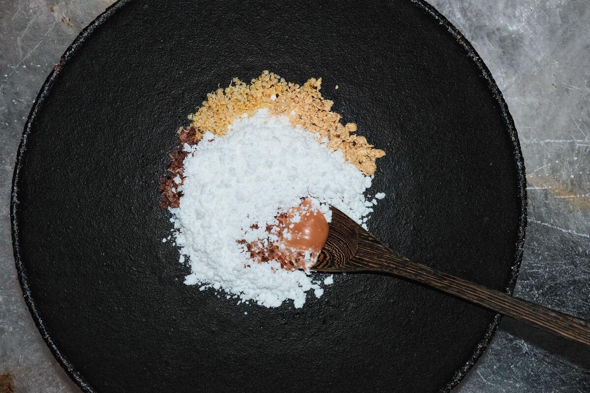 A wooden spoon unearths a chocolate-pudding-like dessert from beneath white and tan powders in a black stone bowl at Meteora