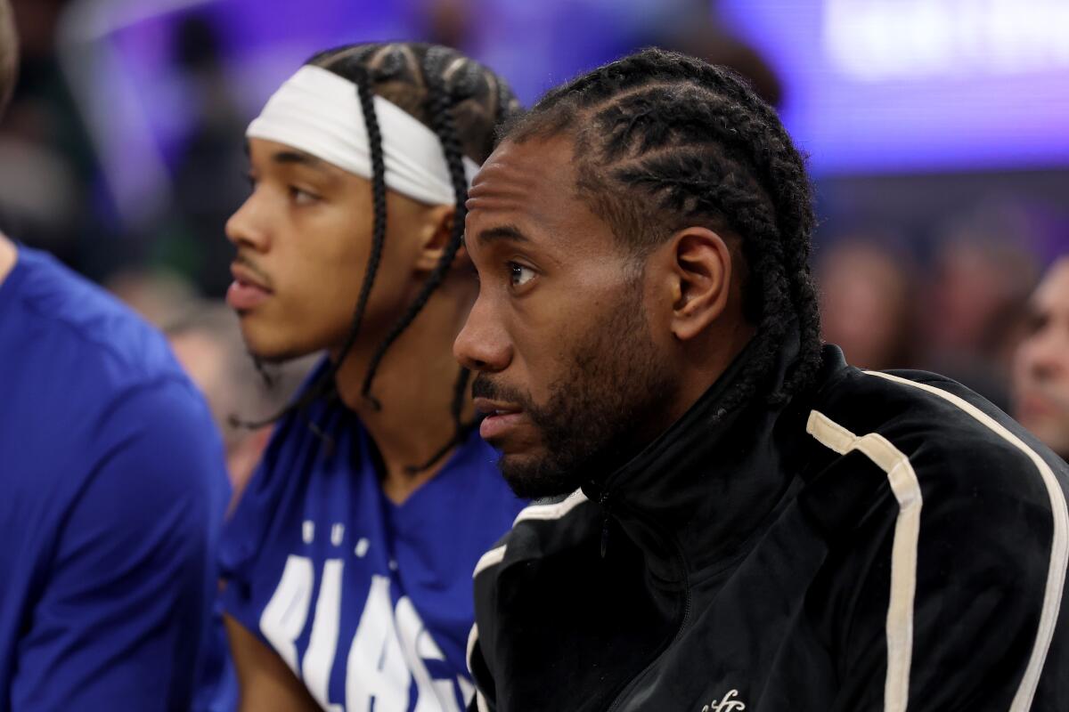 Clippers star Kawhi Leonard sits on the bench in street clothes.