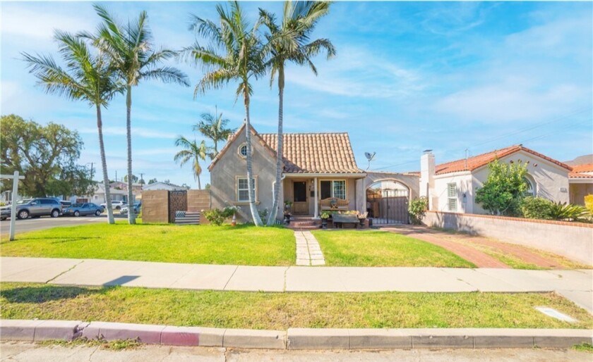 A home with a lawn and palm trees in front and a gate on the right side of the property.