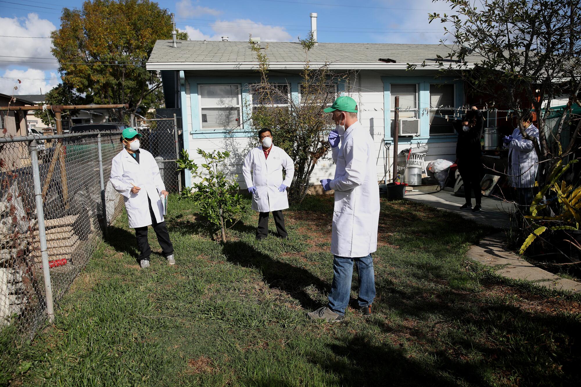 Three people in white lab coats stand in a backyard. 