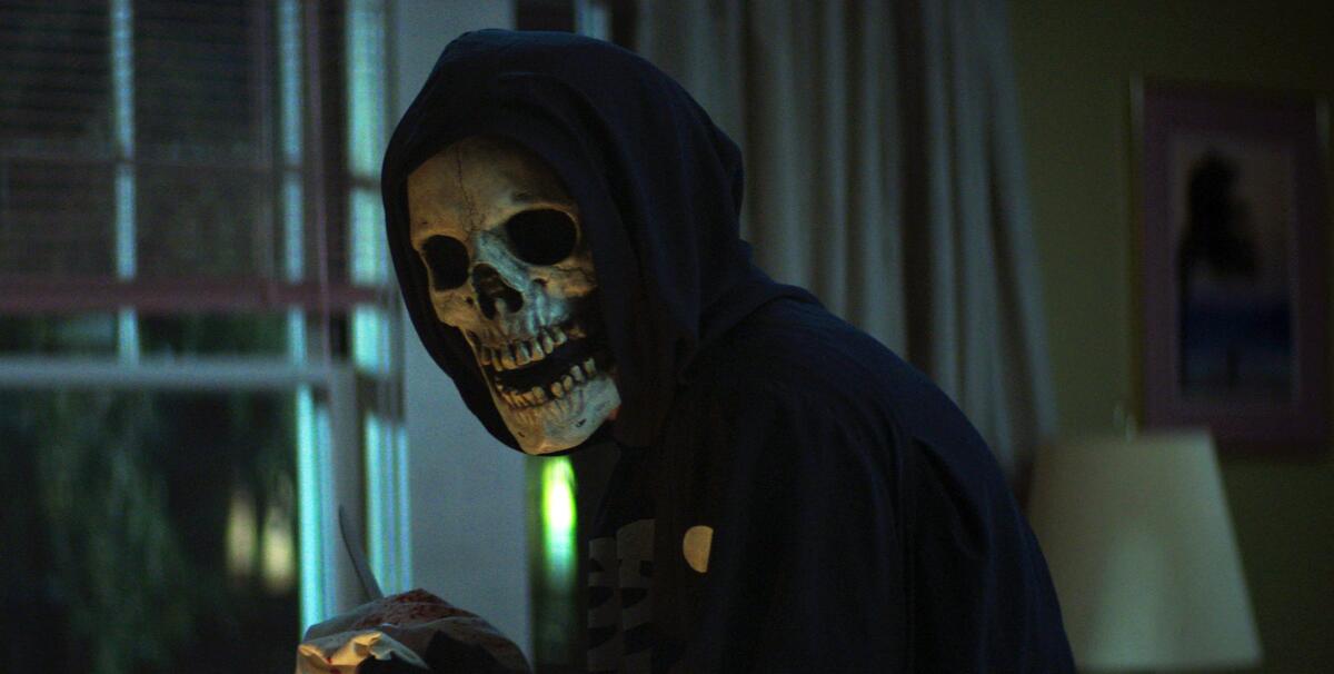 A figure in a skull mask and hoodie in a house at night 