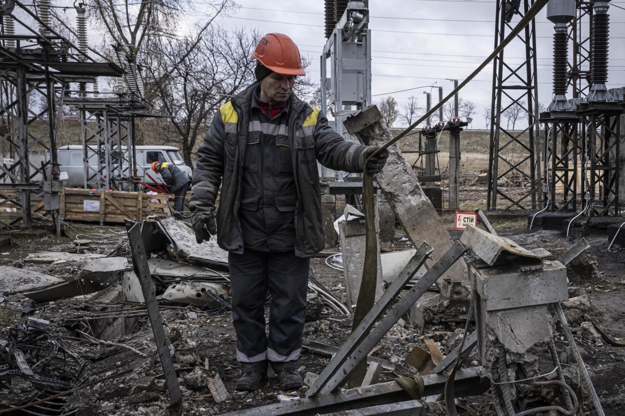 A worker in a helmet and heavy coat stands in the rubble of a power station.