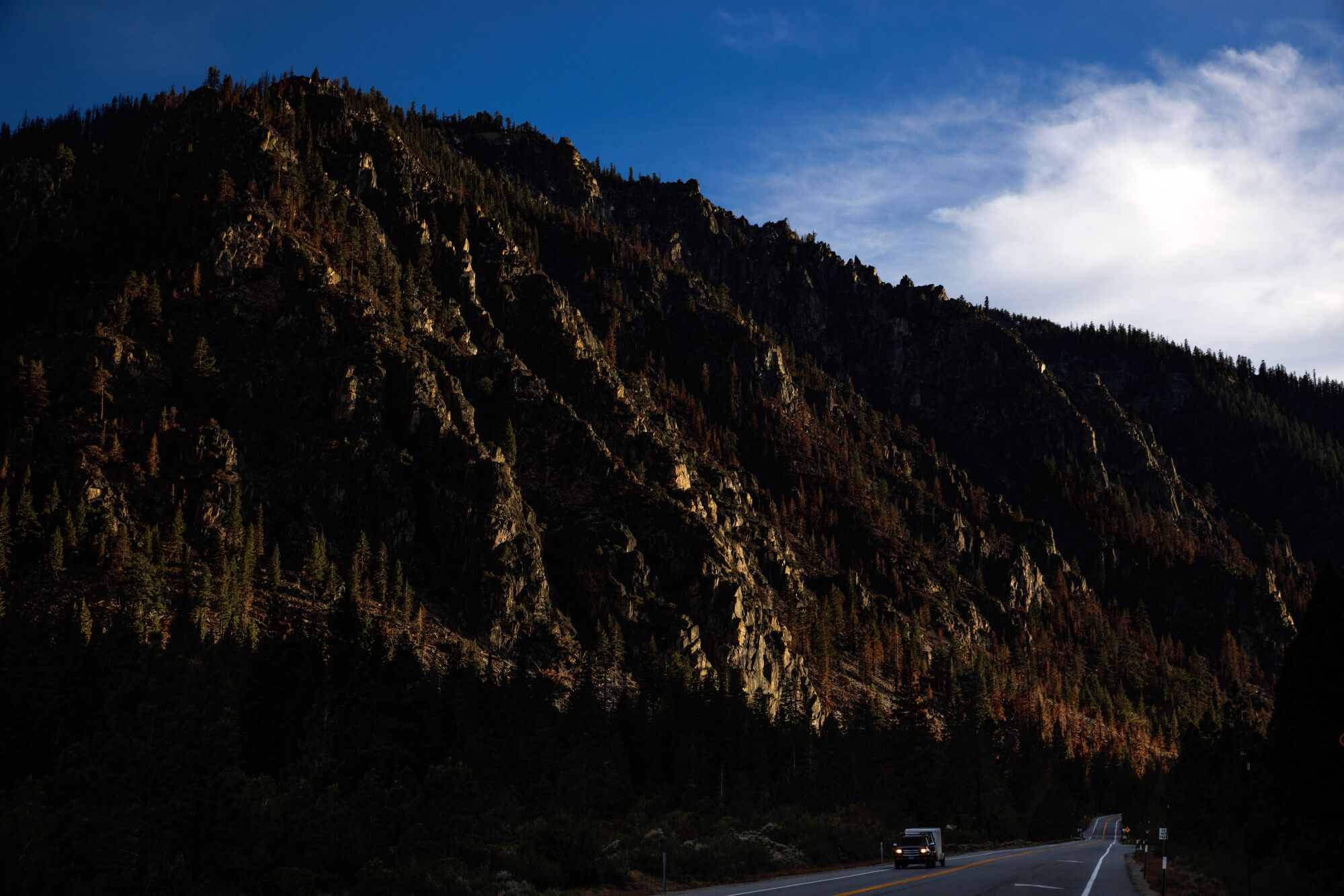 A lone vehicle traveling a highway alongside rocky, mountainous terrain