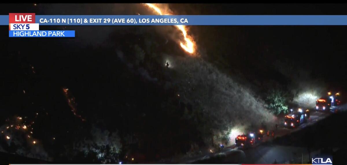 A screenshot of TV news footage shows fire engines next to a hillside with flames burning in the brush