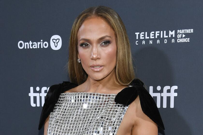 Jennifer Lopez posing in a dress made of mirrored pieces with a capelet over her shoulders