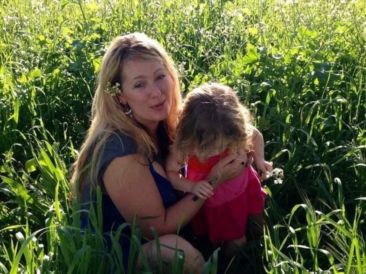 Alaina McLeod, with daughter Feyla as a toddler, crouch amid tall grass.