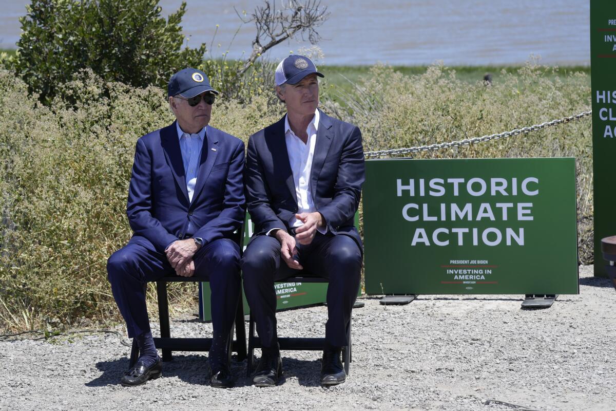 President Biden and California Gov. Gavin Newsom seated next to a sign reading "Historic climate action" at a press event.