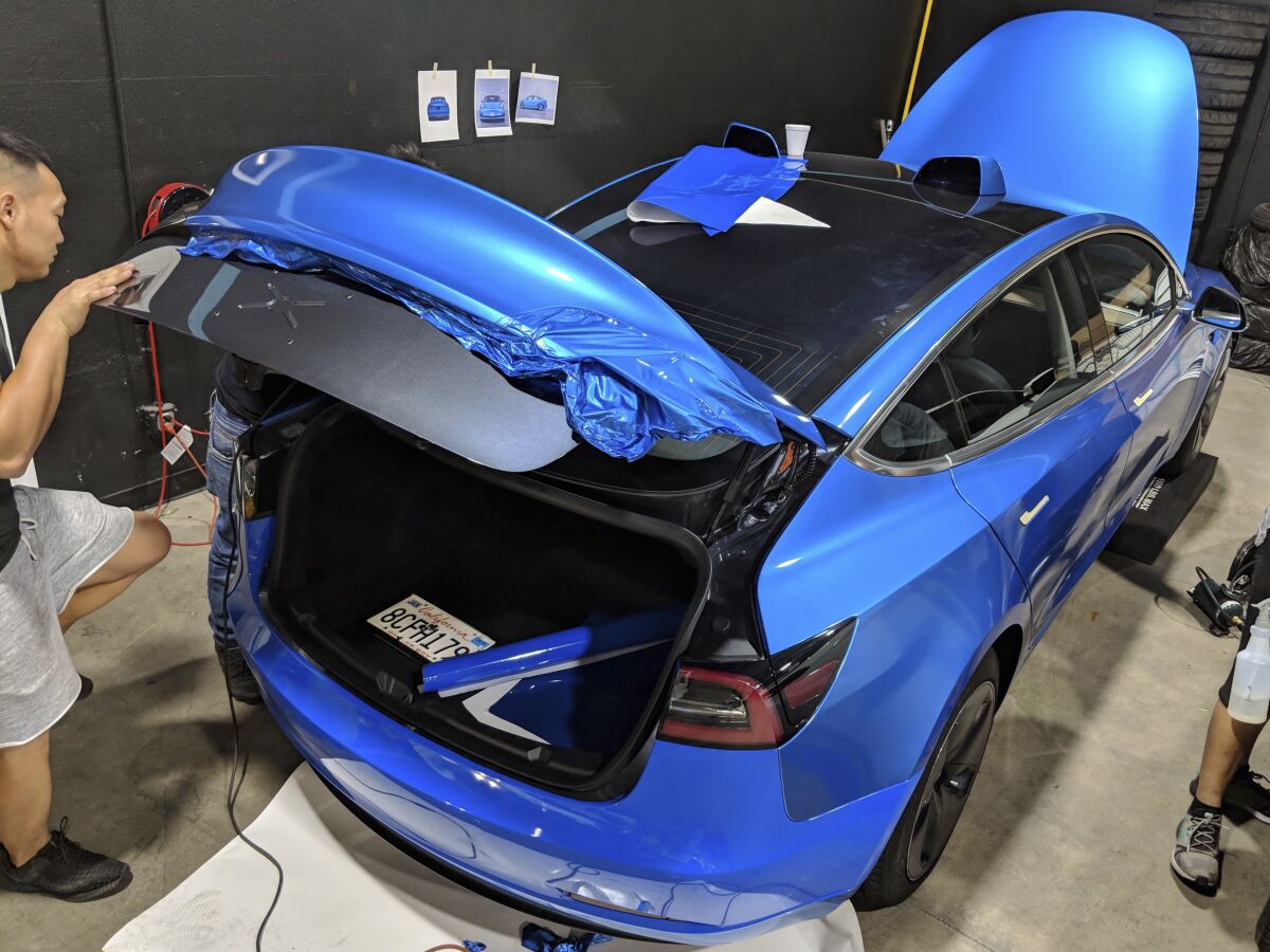 This photo provided by Edmunds shows a car wrap being installed on a Tesla Model 3. The job to apply this metallic light blue vinyl cost about $3,700 at a shop in Southern California. This included parts, labor and an optional ceramic coating for added durability. (Scott Jacobs/Courtesy of Edmunds via AP)